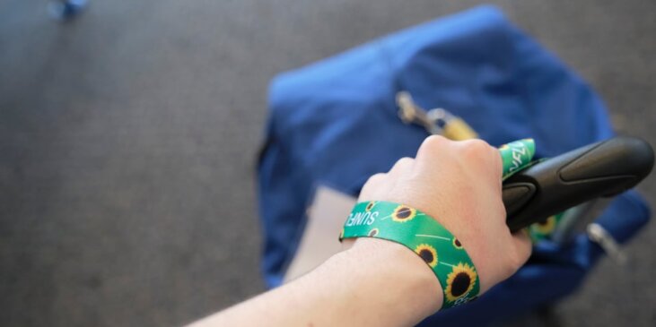 Hand dragging a rolling suitcase with a sunflower bracelet around the traveler’s wrist