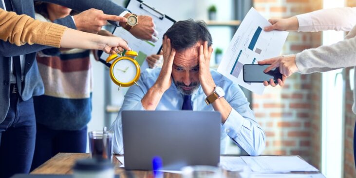 Man sitting at table with laptop, being overwhelmed by different forms of data from people standing next to them.
